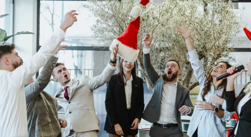 Des employés lancent des bonnets de Père Noël en l'air, célébrant joyeusement leur repas de Noël d'entreprise.