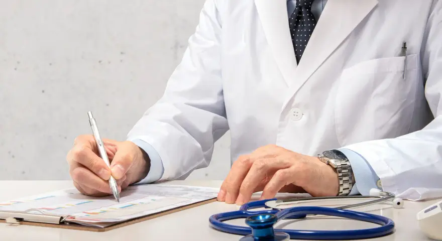 Médecin en blouse blanche rédigeant un rapport, stéthoscope à proximité. Un signalement médecine du travail est en cours.