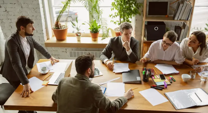 Une équipe discute autour d'une table dans un bureau lumineux, illustrant le concept de **flex office** : collaboration et adaptabilité.