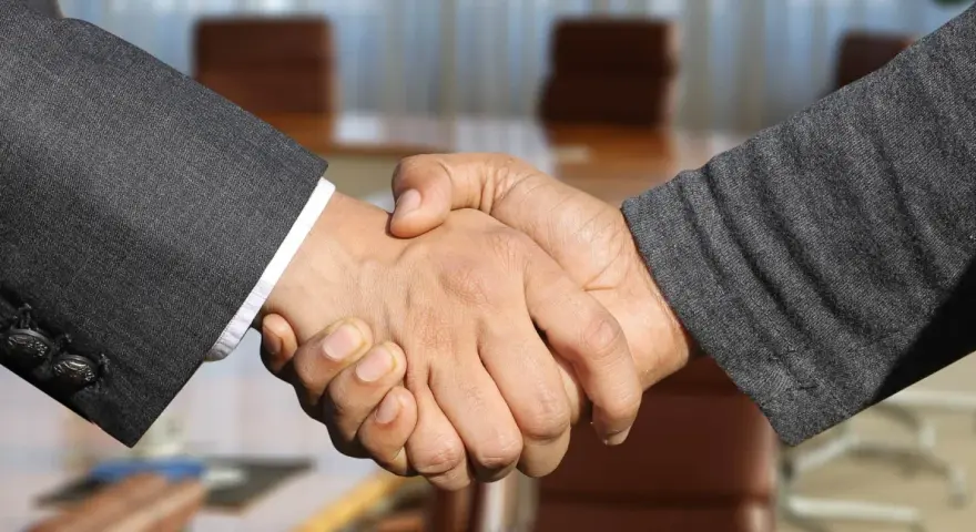 Poignée de main entre deux hommes en costume, scellant un accord. Leurs mains se serrent fermement, symbolisant la confiance et le partenariat.