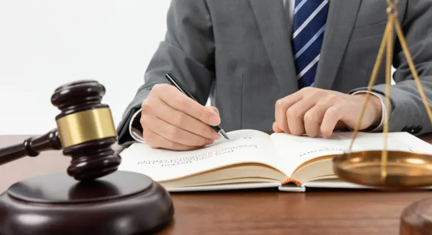 Un avocat en costume écrit dans un livre de droit, marteau de juge et balance de la justice à proximité. Une scène symbolisant l'entrave au CSE.