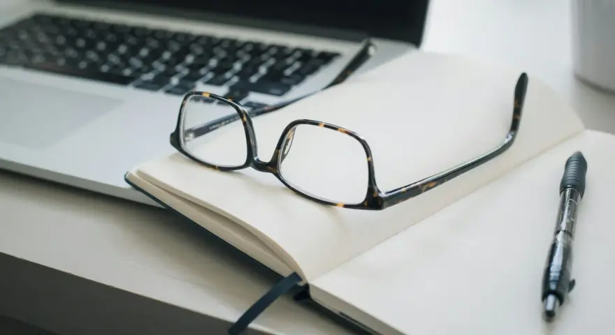 Lunettes sur un carnet ouvert, stylo et ordinateur portable. Idéal pour un congé formation professionnelle dans le privé, pour planifier son avenir.
