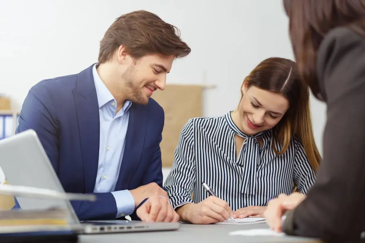 Un homme et une femme souriants discutent d'un contrat de travail étudiant. Un ordinateur portable est visible sur la table.