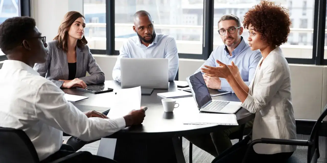 Réunion d'équipe discutant d'un bon de délégation CSE. Des collaborateurs échangent autour d'une table avec des ordinateurs portables et des documents.