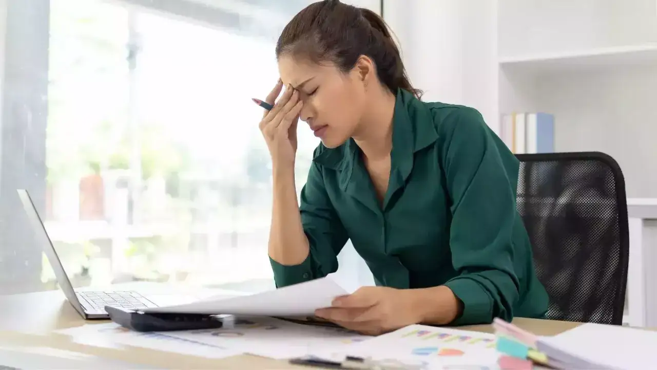Femme stressée au bureau, le front froissé, tenant un stylo. Elle semble préoccupée par un motif de licenciement.
