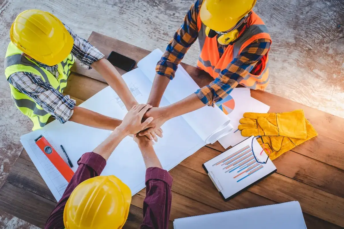 Équipe d'ouvriers en casque, mains jointes sur des plans. Le ssct cse est au cœur de leur projet.