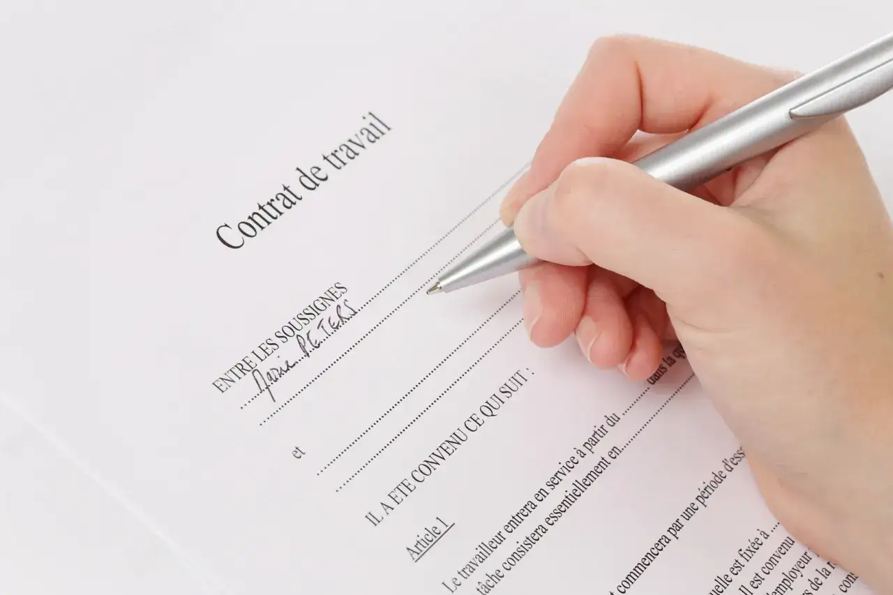 Main tenant un stylo pour signer un contrat de travail CDI. Le document est intitulé 